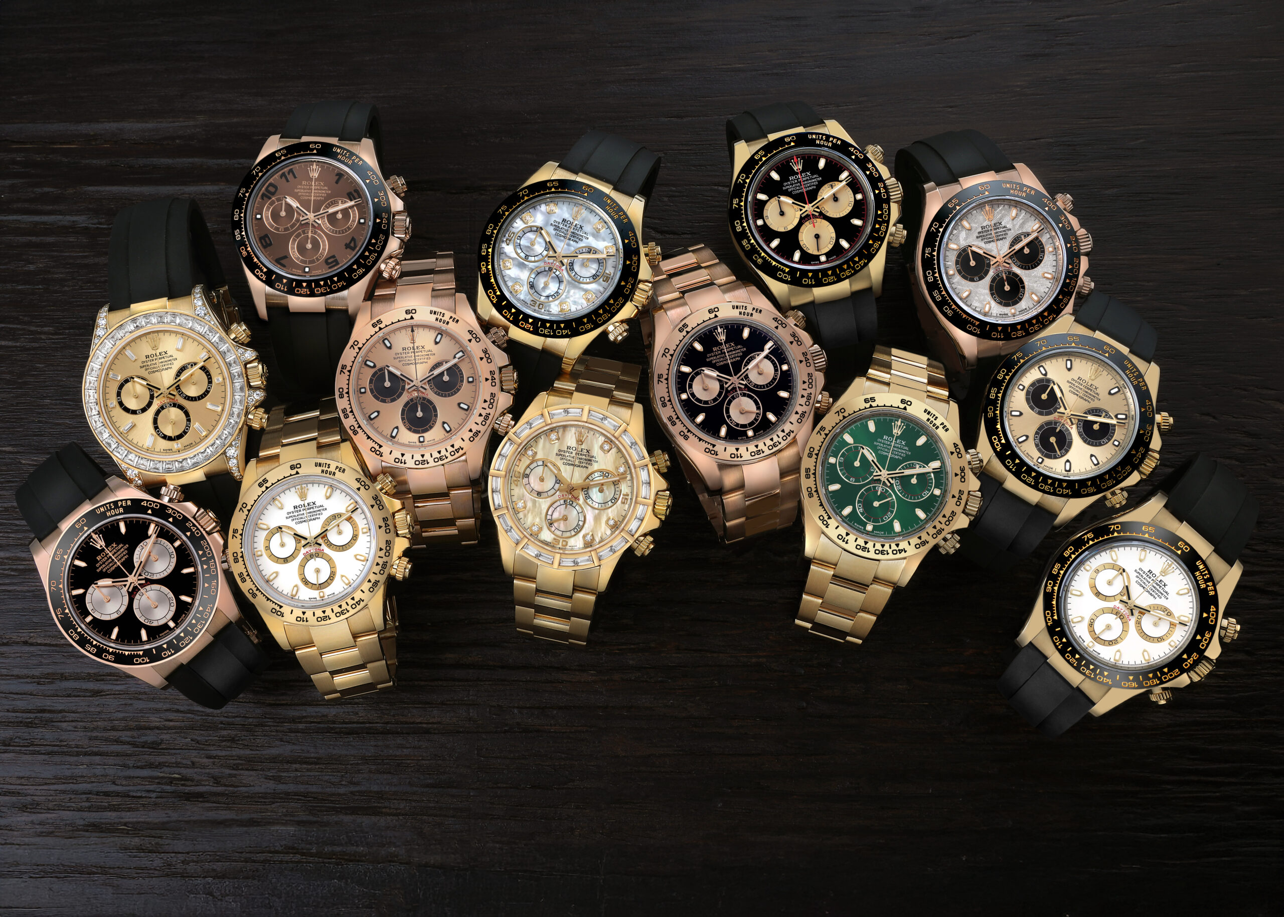A collection of luxury Rolex Daytona chronographs in various proprietary materials, including 18k yellow gold and Everose gold, resting on a dark wooden surface.