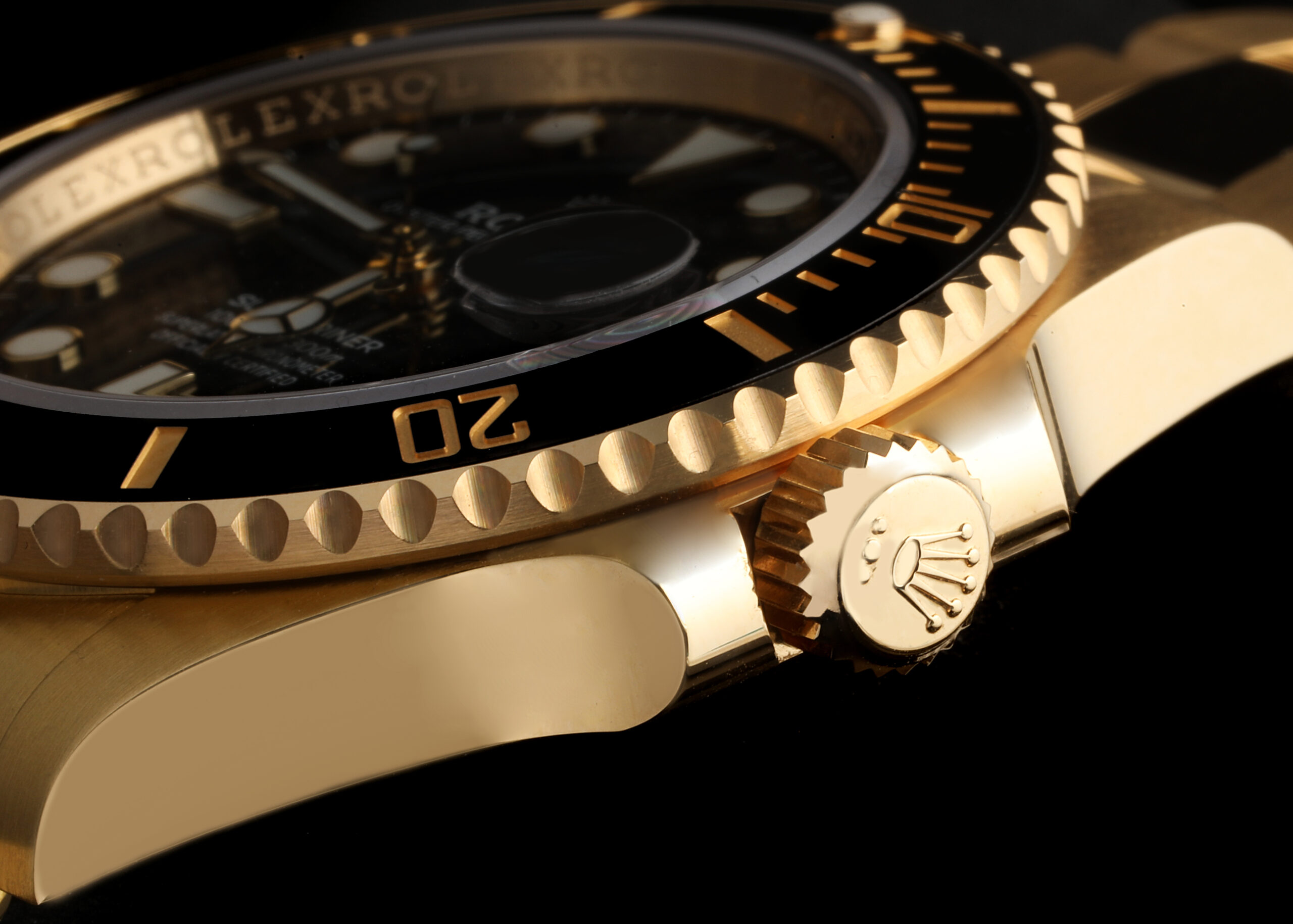 Macro shot of an 18k yellow gold Rolex Submariner winding crown featuring the raised Rolex coronet logo.