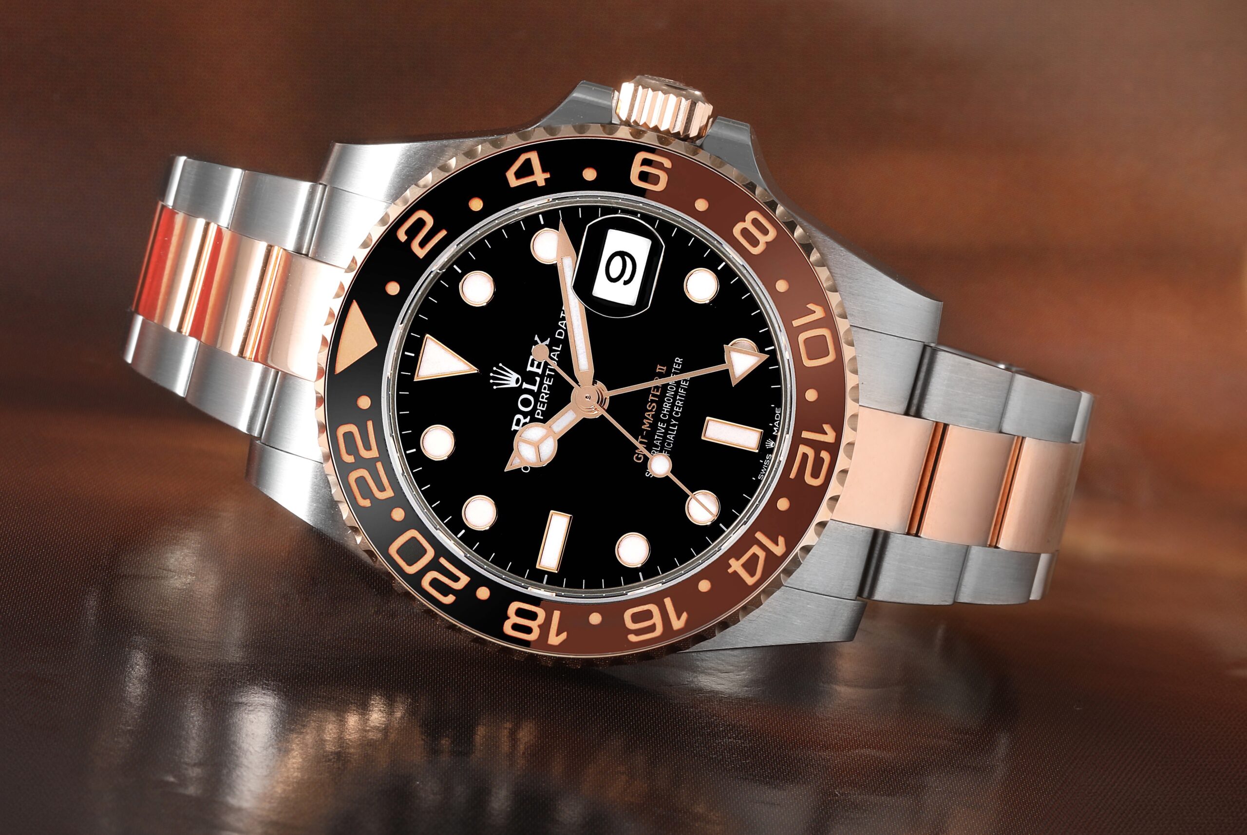 A studio shot of a two-tone Rolex GMT-Master II 126711CHNR watch with an Everose gold and steel bracelet, a black dial, and a brown and black ceramic bezel.