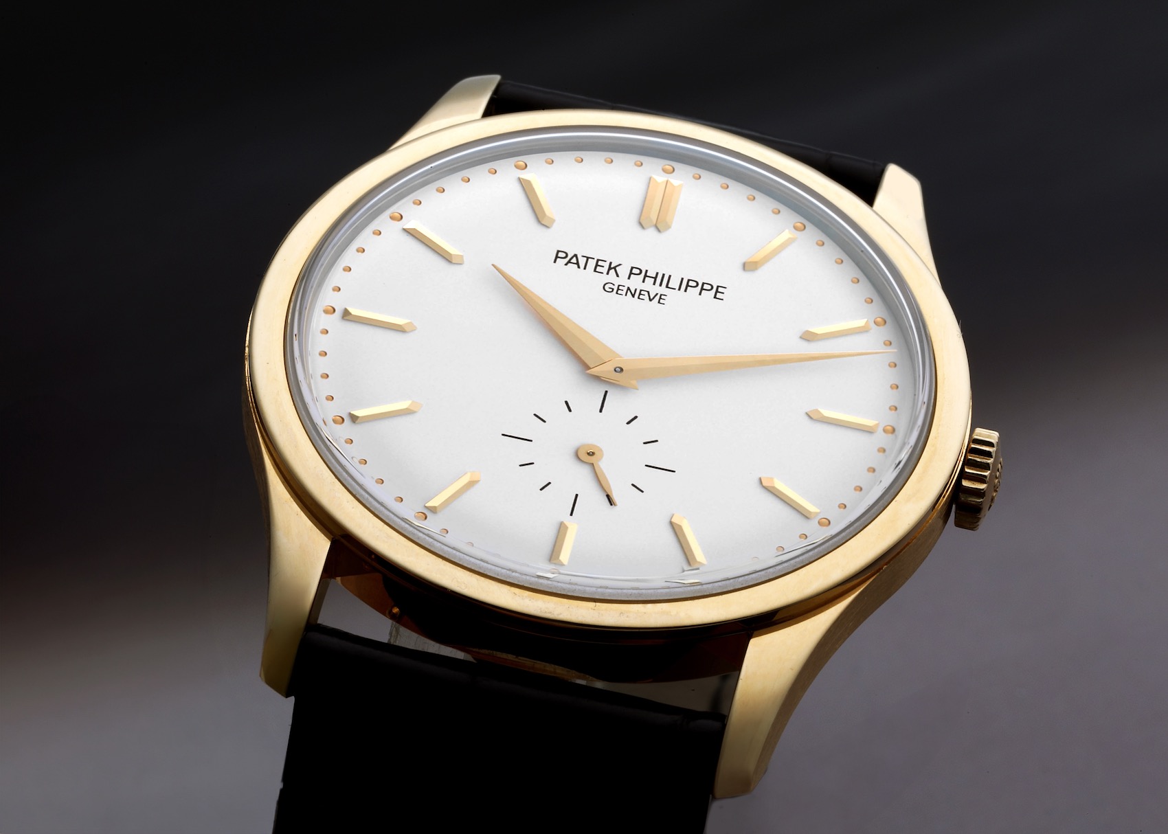 A macro shot of a Patek Philippe Calatrava 5196J in yellow gold, showcasing its clean silver dial, minimalist gold hour markers, and a small seconds sub-dial.
