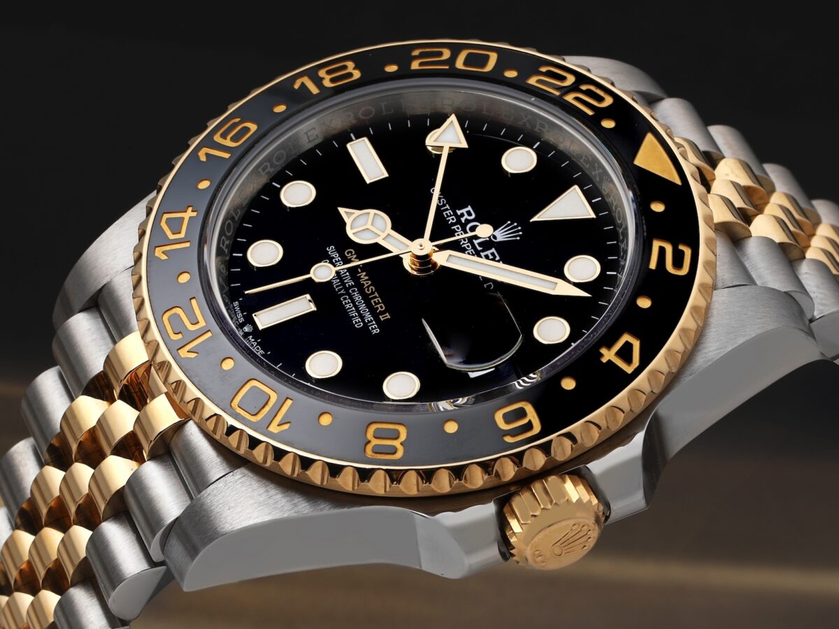 A detailed shot of a two-tone Rolex GMT-Master II 126713, contrasting steel with yellow gold. The Mercedes hour hand is rendered in polished yellow gold, matching the bezel and bracelet details.