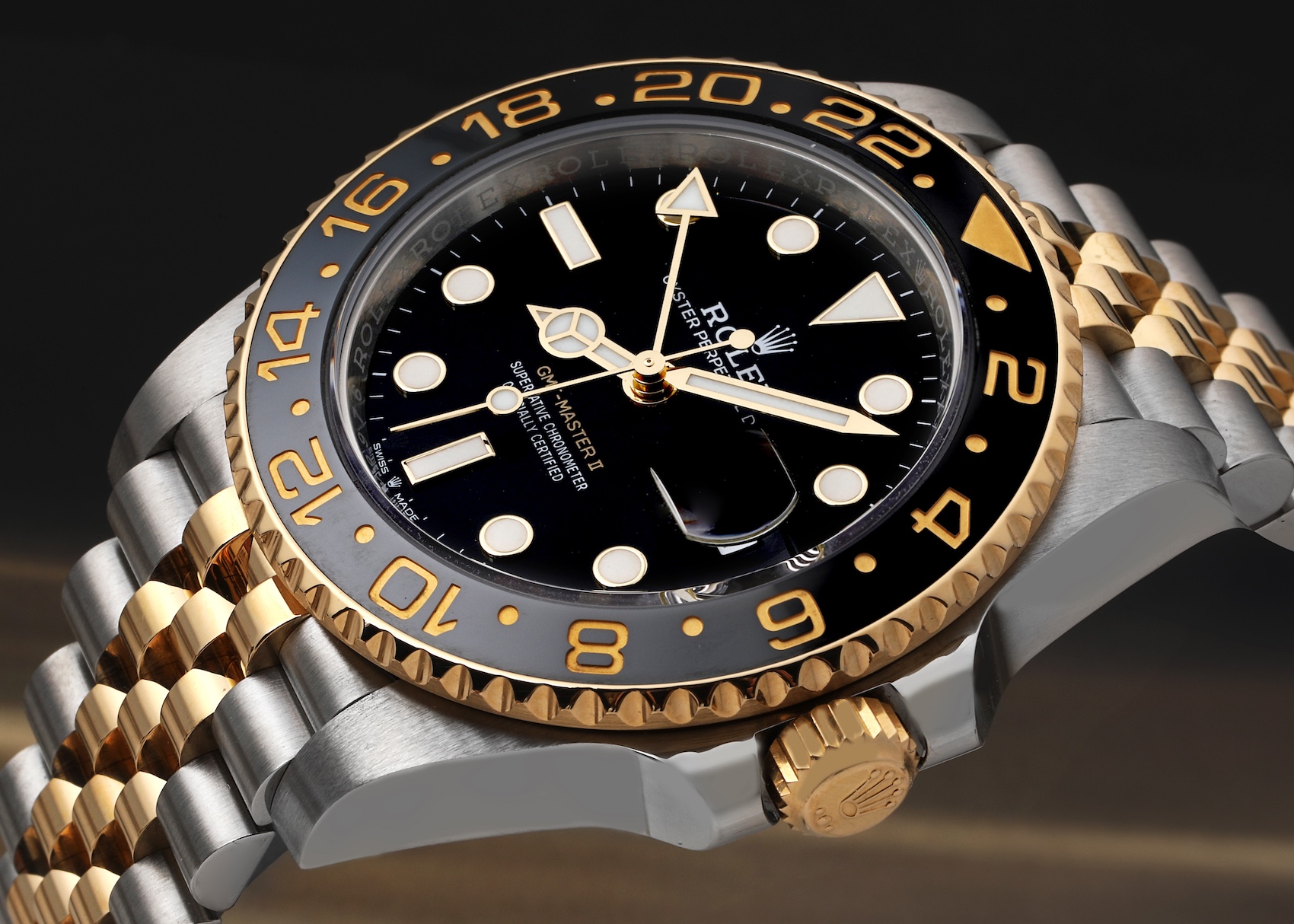 A detailed shot of a two-tone Rolex GMT-Master II 126713, contrasting steel with yellow gold. The Mercedes hour hand is rendered in polished yellow gold, matching the bezel and bracelet details.