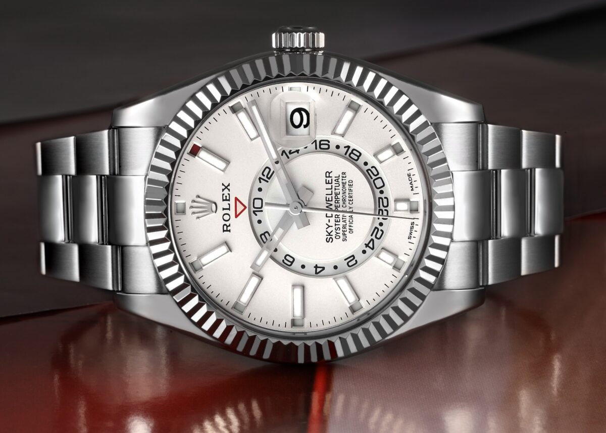 A front-facing macro shot of a stainless steel Rolex Sky-Dweller with a white dial, clearly displaying the off-center 24-hour disc for the dual time zone function.