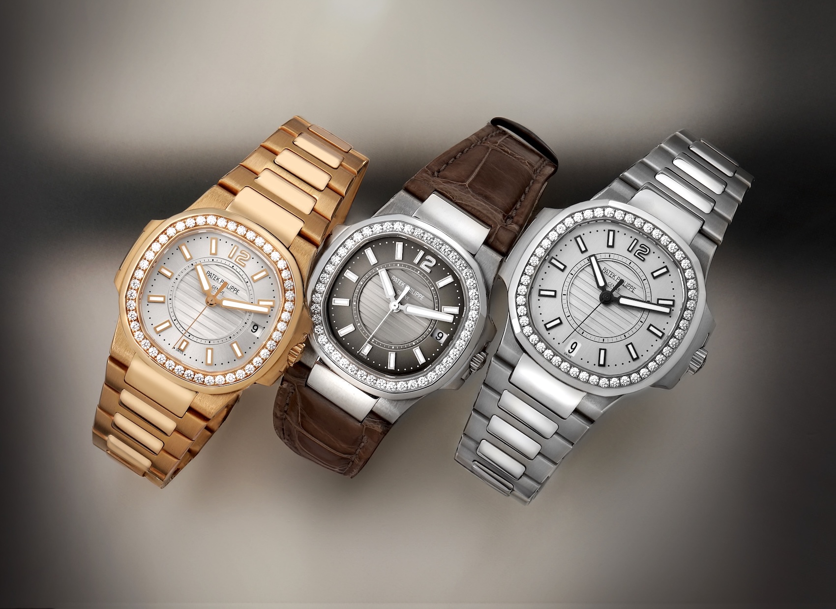 A lineup of three Patek Philippe Nautilus ladies watches. Left: Rose gold with white dial and bracelet. Center: White gold with dark grey dial and brown leather strap. Right: Stainless steel with white dial and bracelet. All feature diamond bezels.