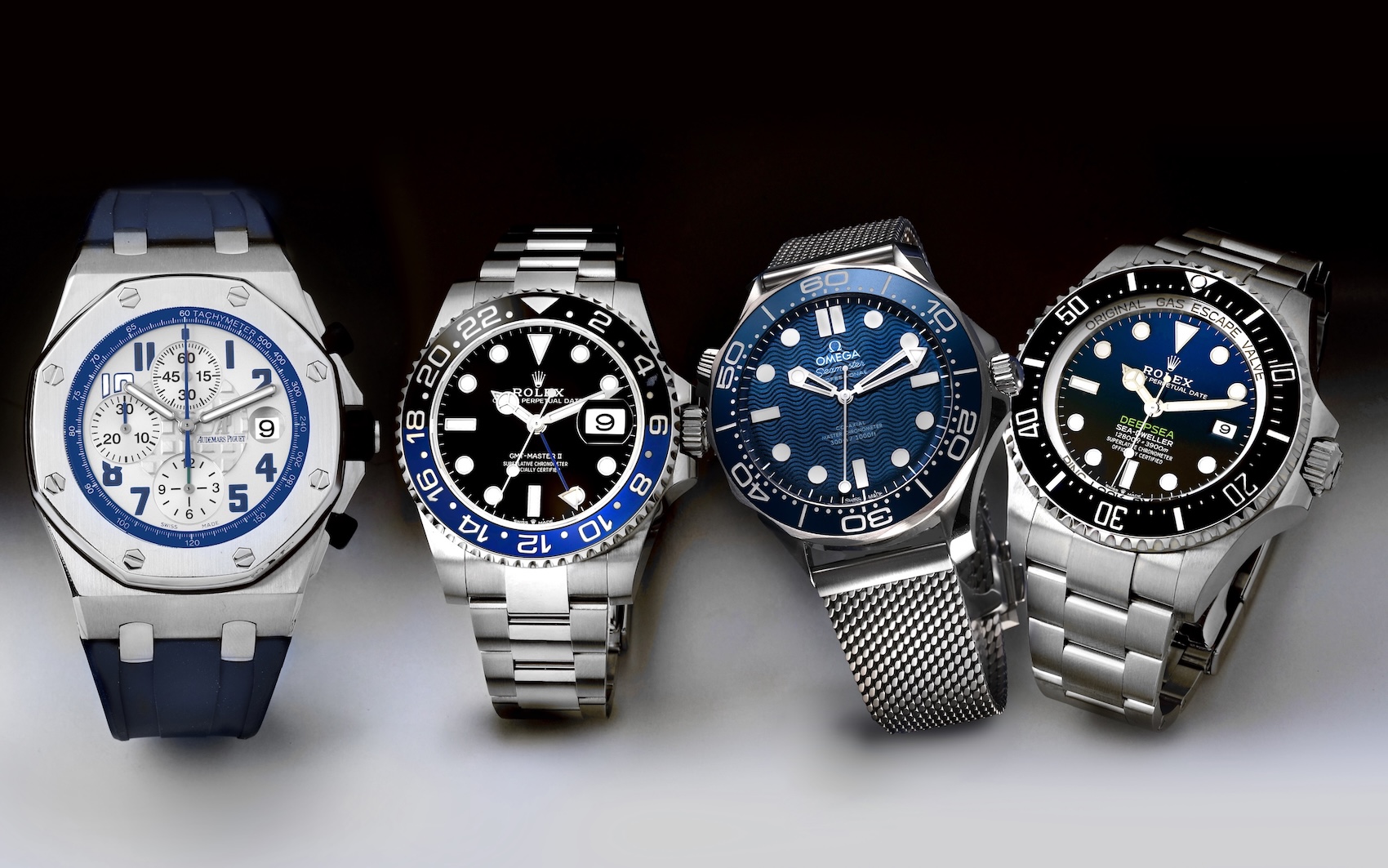 A collection of four luxury mens sports watches including an Audemars Piguet Royal Oak Offshore, Rolex GMT-Master II Batman, Omega Seamaster, and Rolex Deepsea.