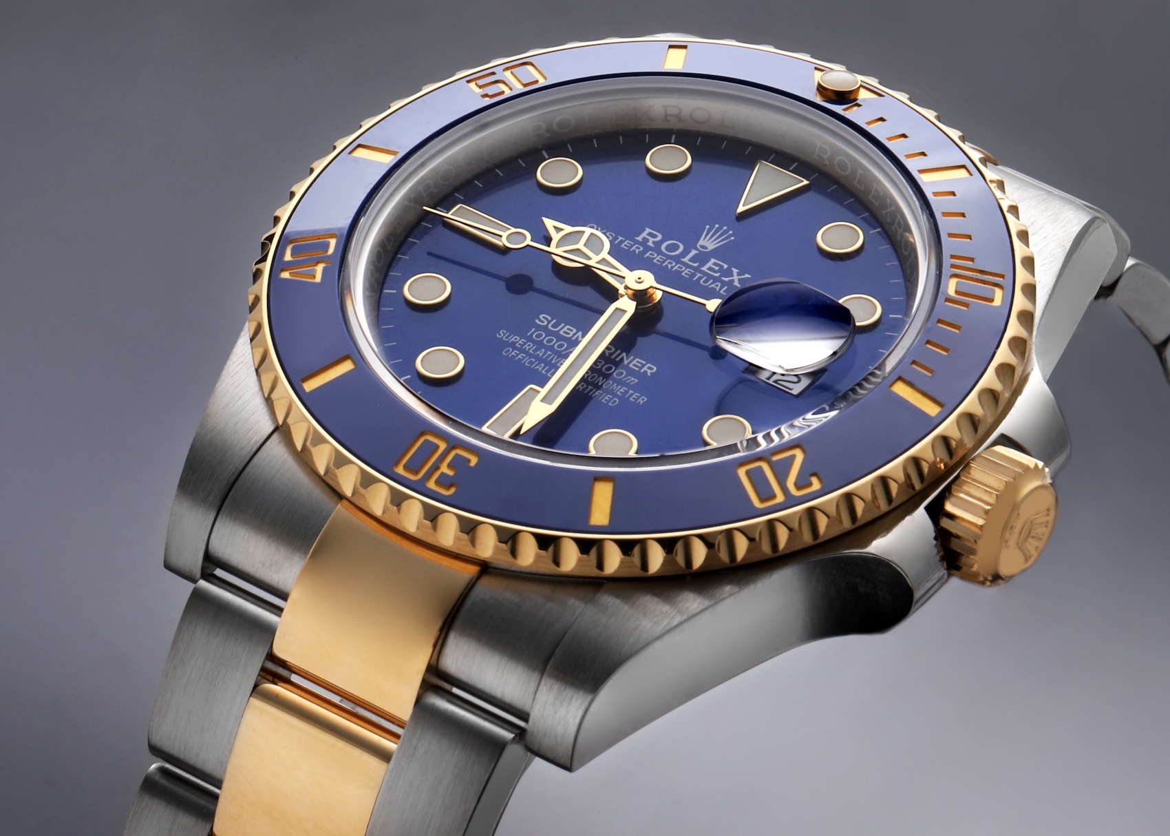 Angled macro profile shot of a Rolex Submariner 41 two-tone watch showing the rich blue sunburst dial, blue ceramic bezel, and gold center links.