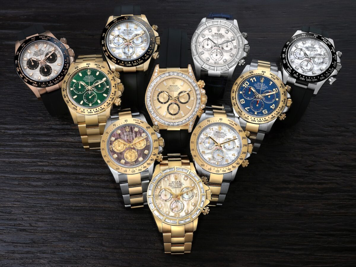 A diverse collection of luxury Rolex Cosmograph Daytona watches in yellow gold, rose gold, and white gold displayed on a dark wooden surface.