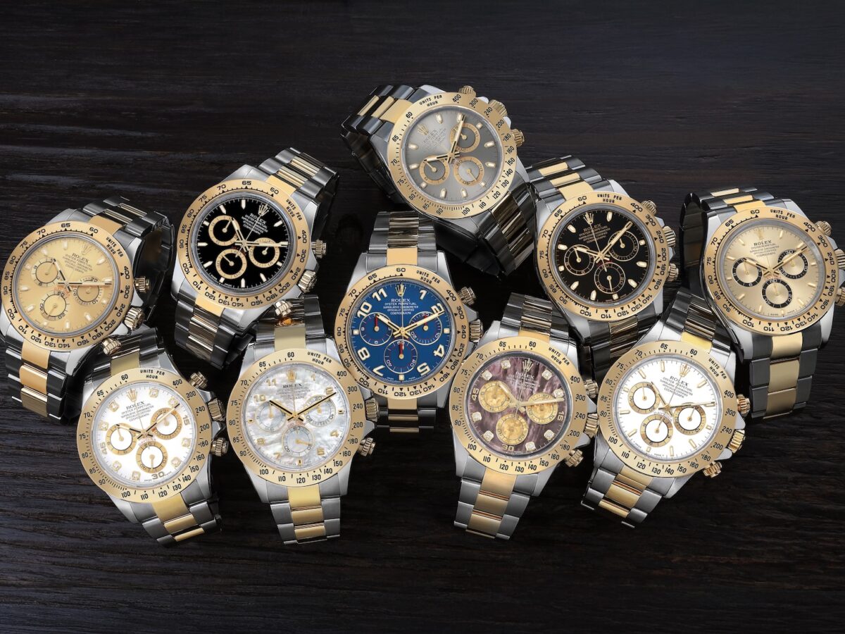 A curated collection of multiple luxury Rolex Cosmograph Daytona two-tone steel and yellow gold watches displayed on a dark rustic wooden surface.