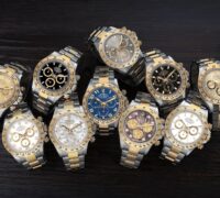 A curated collection of multiple luxury Rolex Cosmograph Daytona two-tone steel and yellow gold watches displayed on a dark rustic wooden surface.