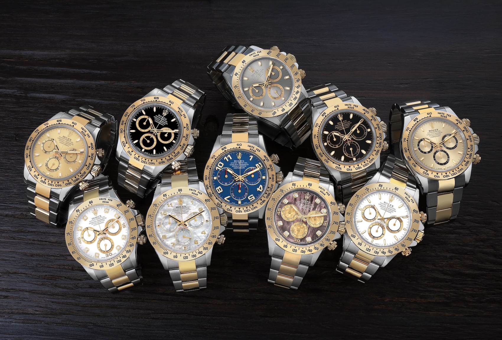 A curated collection of multiple luxury Rolex Cosmograph Daytona two-tone steel and yellow gold watches displayed on a dark rustic wooden surface.