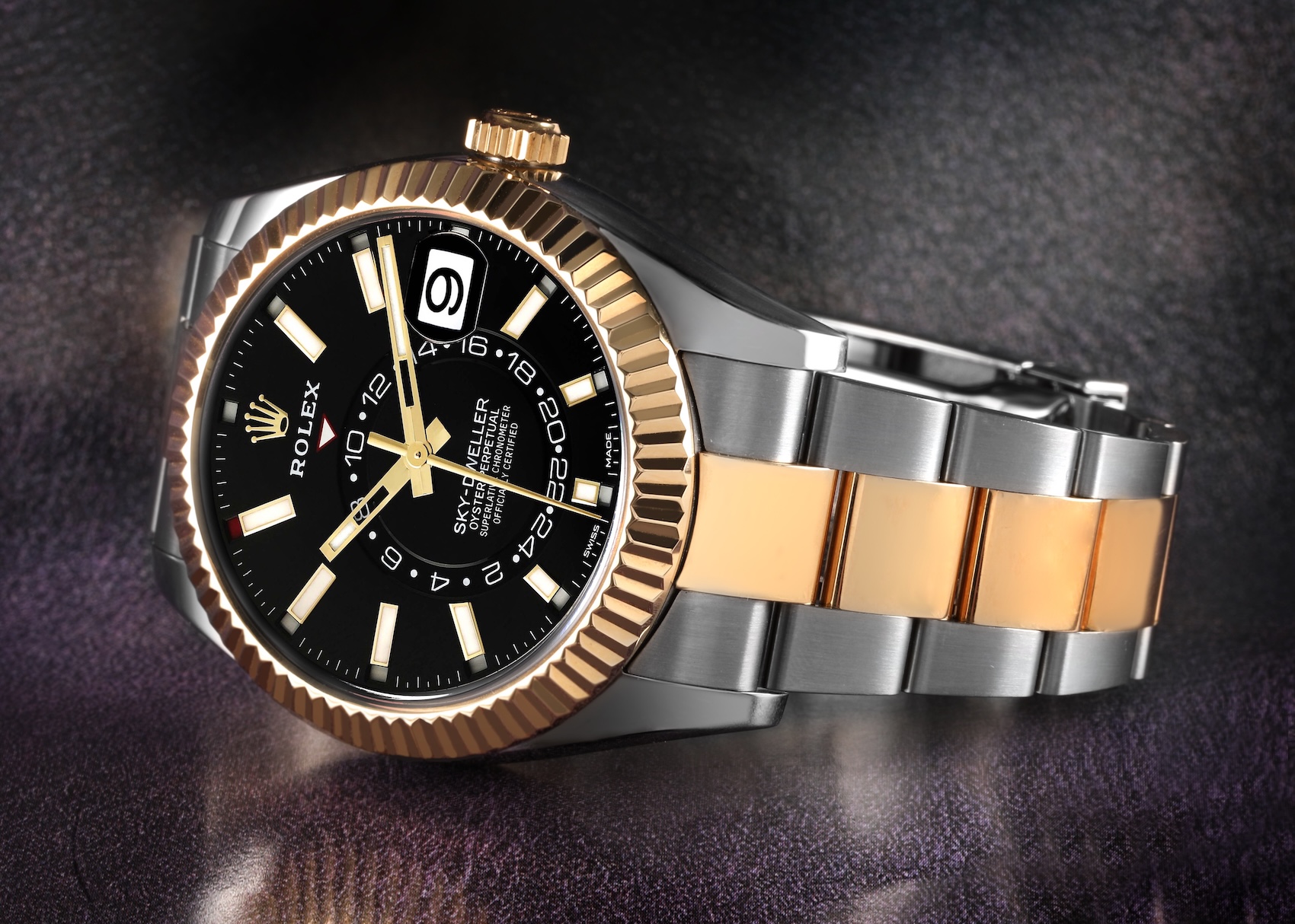 Macro photograph of a Rolex Sky-Dweller two-tone stainless steel and yellow gold annual calendar watch featuring a black dial and fluted command bezel.
