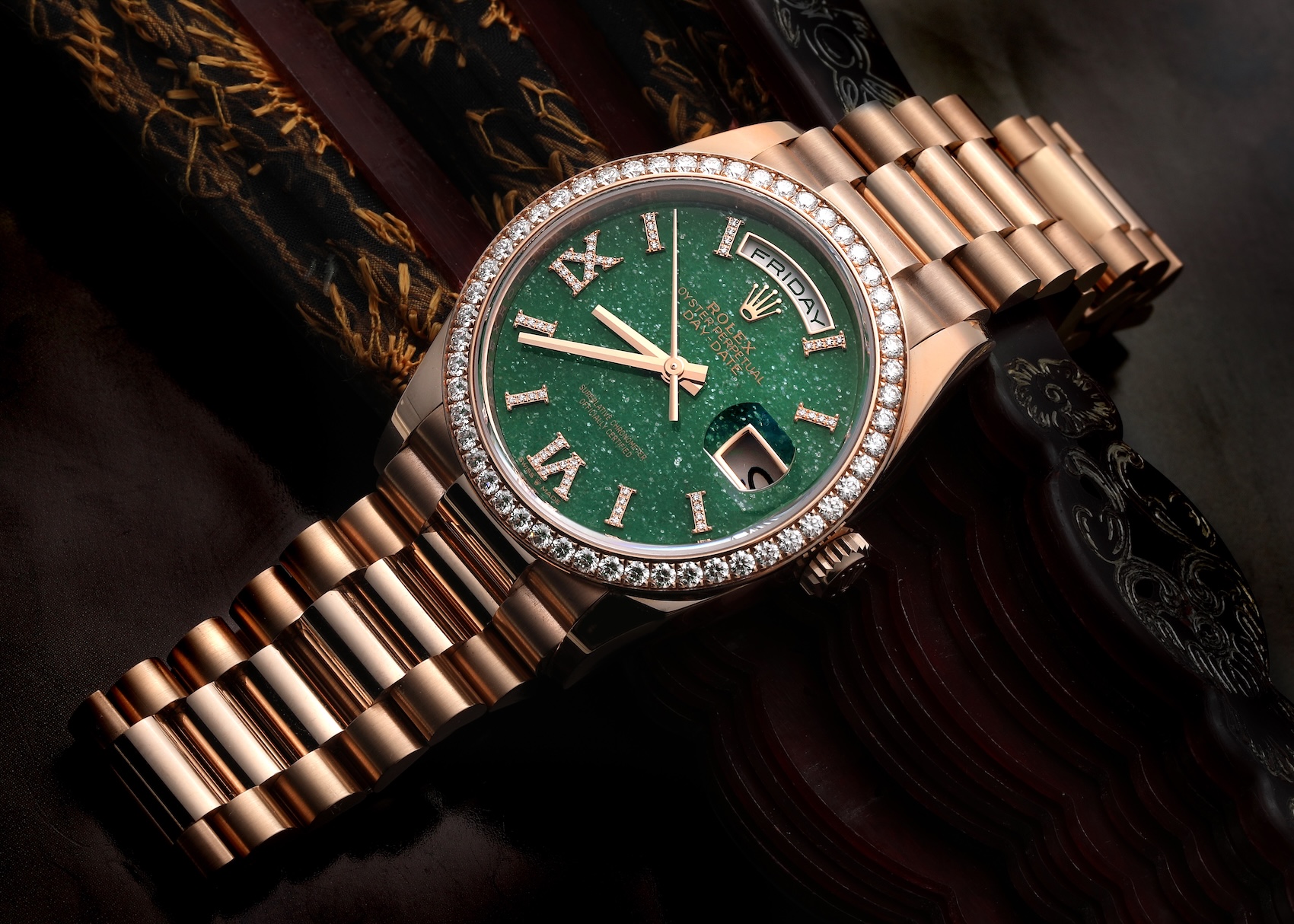 Rolex Day-Date 36 Ref 128345 in Everose gold featuring a sparkling green aventurine dial, diamond-set Roman numerals, and a diamond bezel resting on a dark wooden surface.