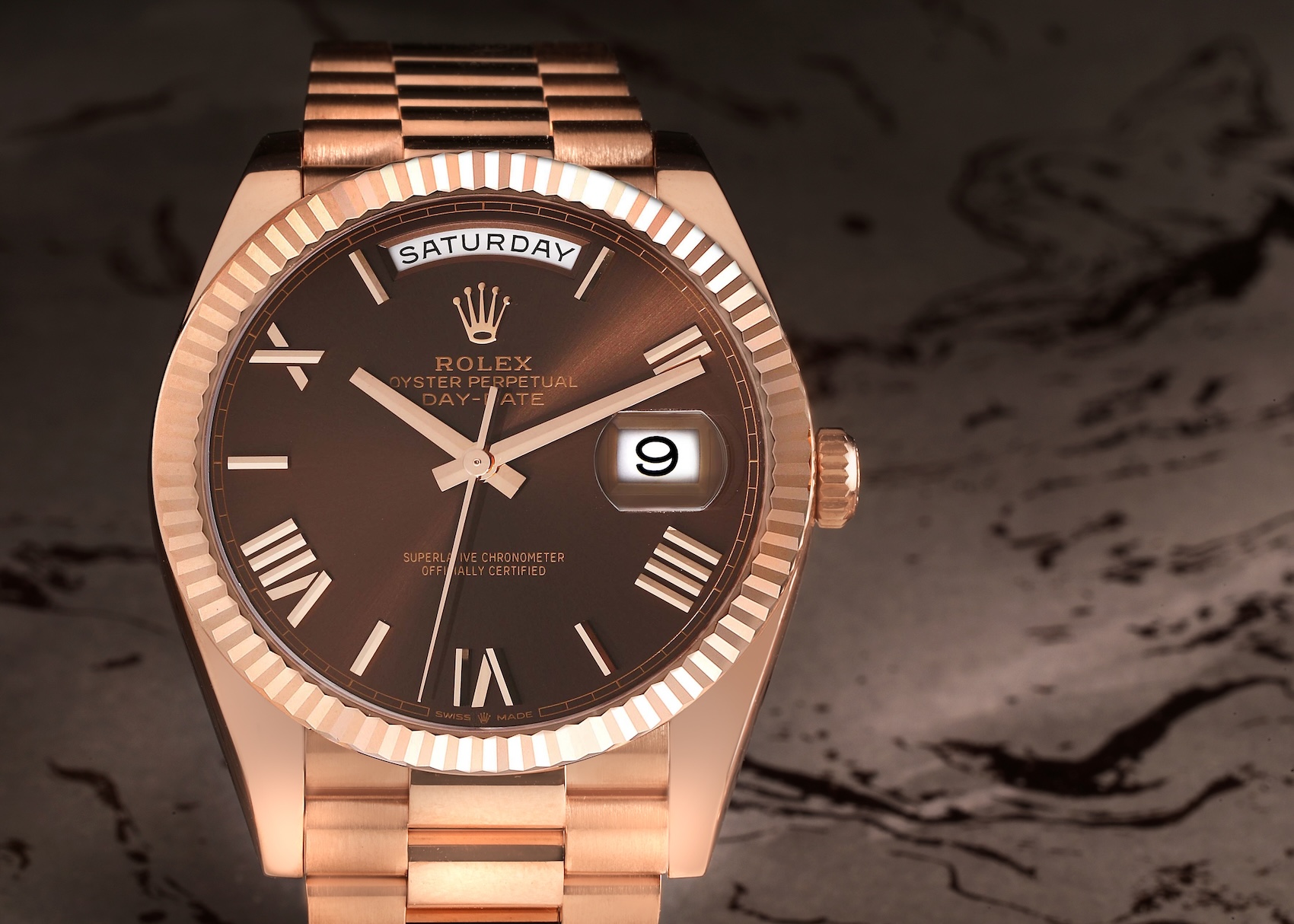 Close up of a Rolex Day-Date 40 Ref 228235 in 18k Everose gold featuring a chocolate sunray dial, faceted rose gold Roman numerals, and a fluted bezel.