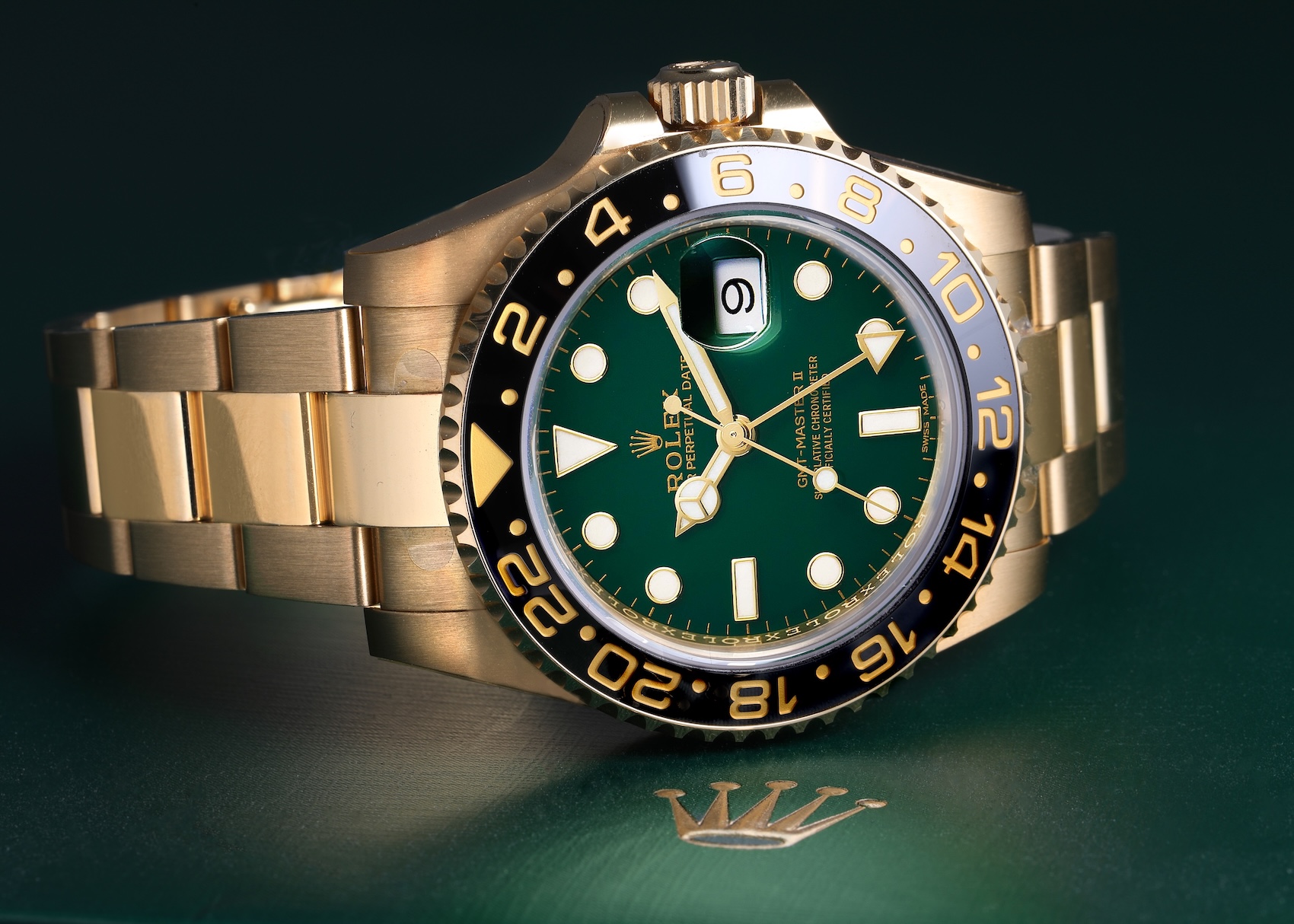Rolex GMT-Master II 116718 in 18k yellow gold resting on a green Rolex box, showcasing its 50th-anniversary green dial and black ceramic bezel.