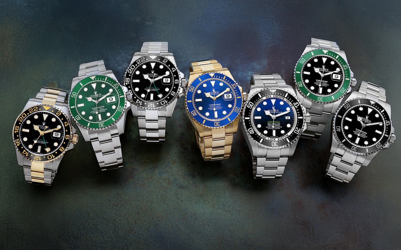 Seven Rolex professional sports watches, including Submariner, GMT-Master II, and Deepsea models in steel, two-tone, and yellow gold, arranged in a semi-circle on a dark surface.
