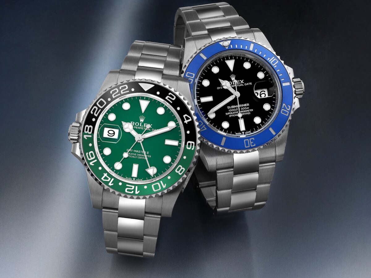 A perspective shot of two current Rolex sports watches angled toward each other: on the left, the left-handed green-bezel "Sprite" GMT-Master II (126720VTNR), and on the right, the blue-bezel "Cookie Monster" Submariner (126619LB), highlighting their distinct aesthetics and configurations.