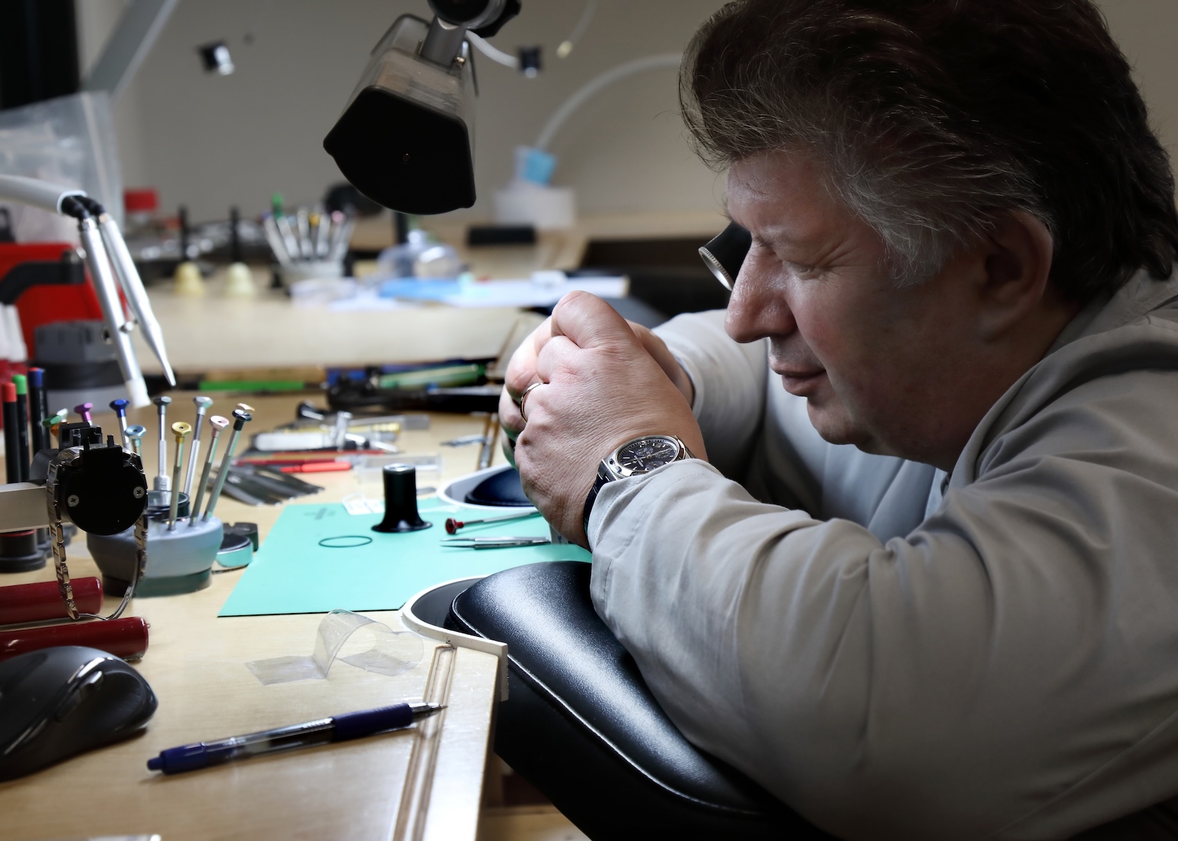An expert watchmaker at Top Quality Designer Watch Shop using a loupe at a workbench to carefully inspect an open mechanical watch movement.